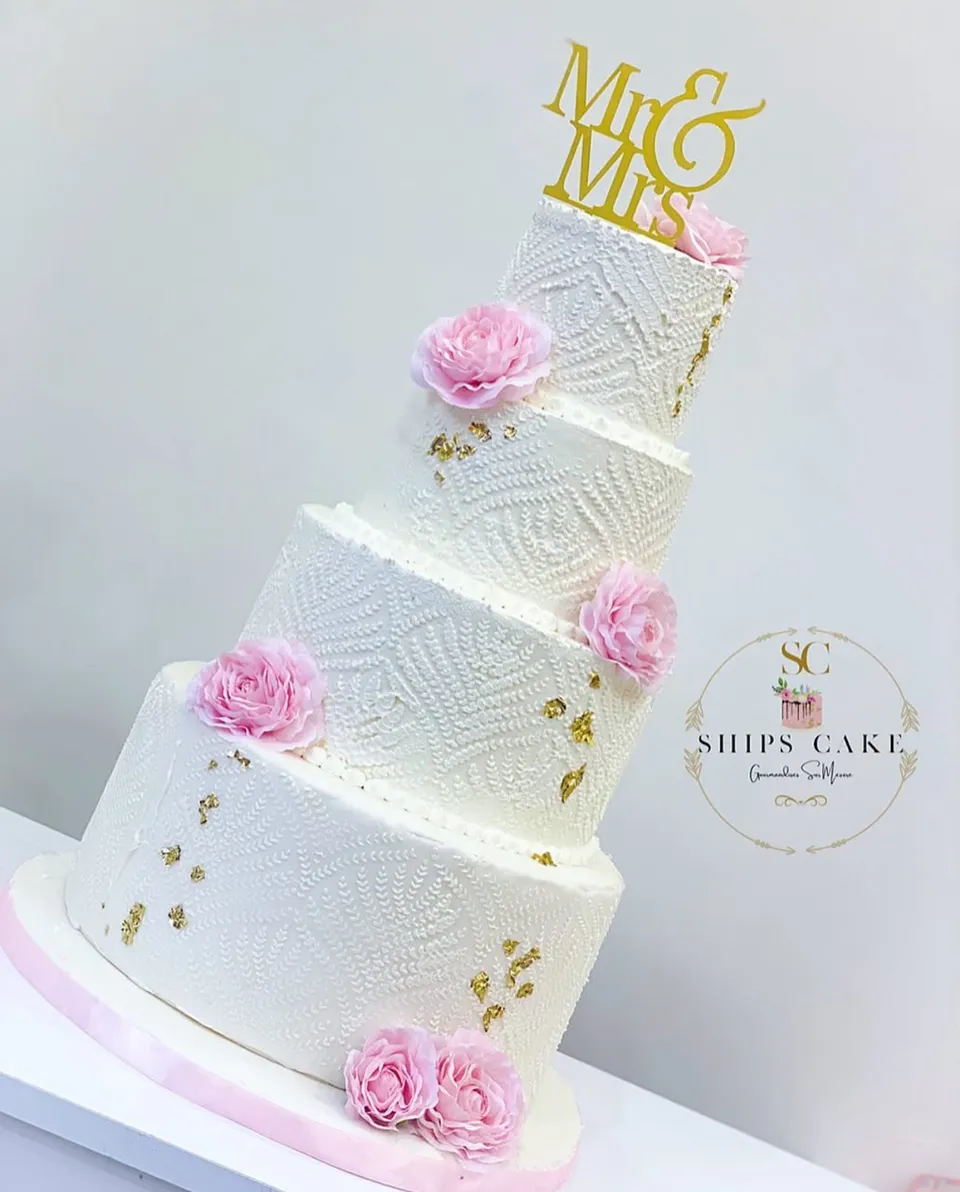 Four-tier wedding cake with textured white icing, pink roses and flecks of gold