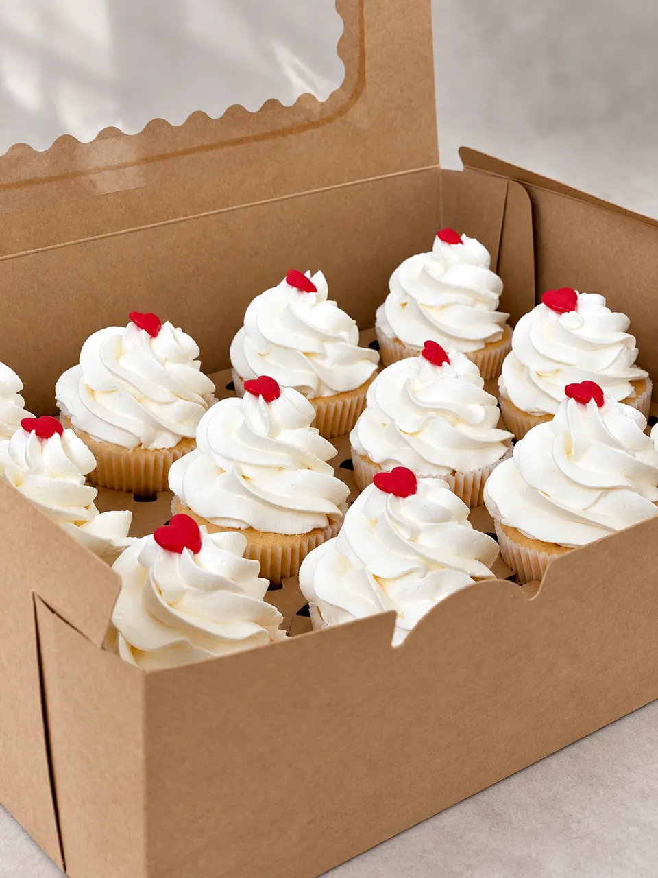 Box of twelve cupcakes with white frosting, each topped with a small red heart