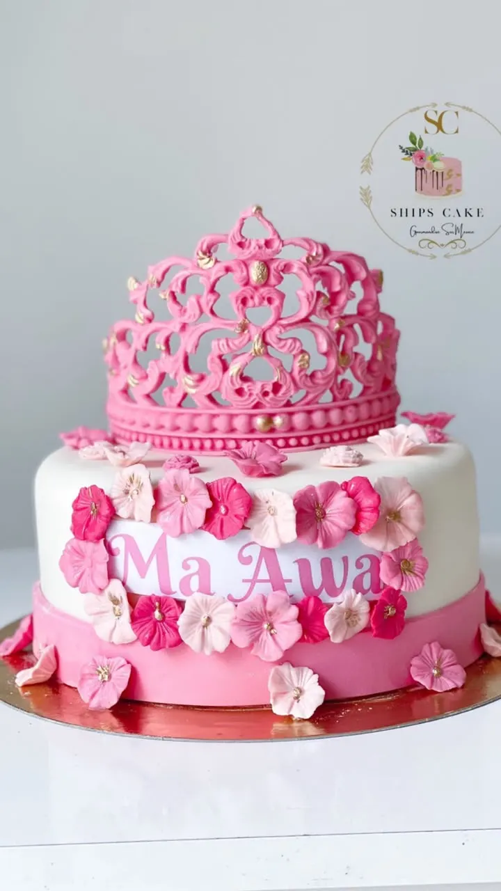 Two-tier pink and white cake with a crown and sugar flowers