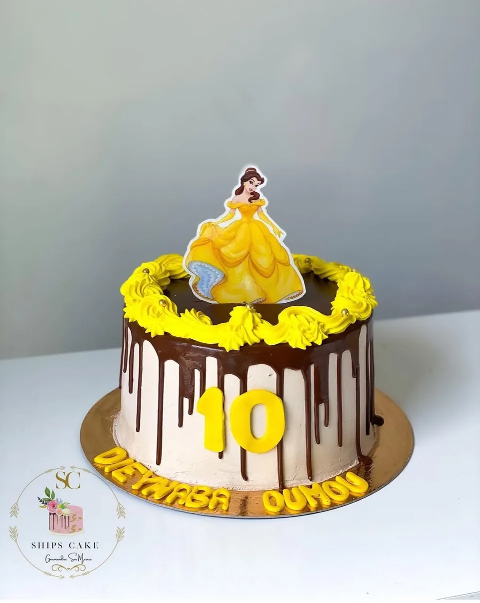 Chocolate drip cake with yellow rosettes and a Disney princess in a yellow gown