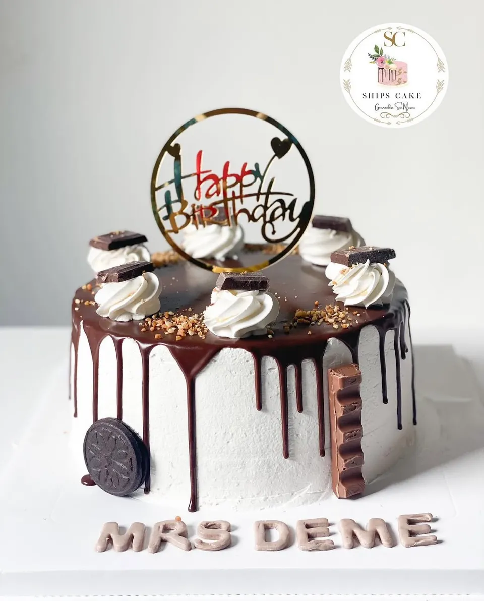 White buttercream cake with a chocolate drip, whipped cream, chocolate squares and biscuits